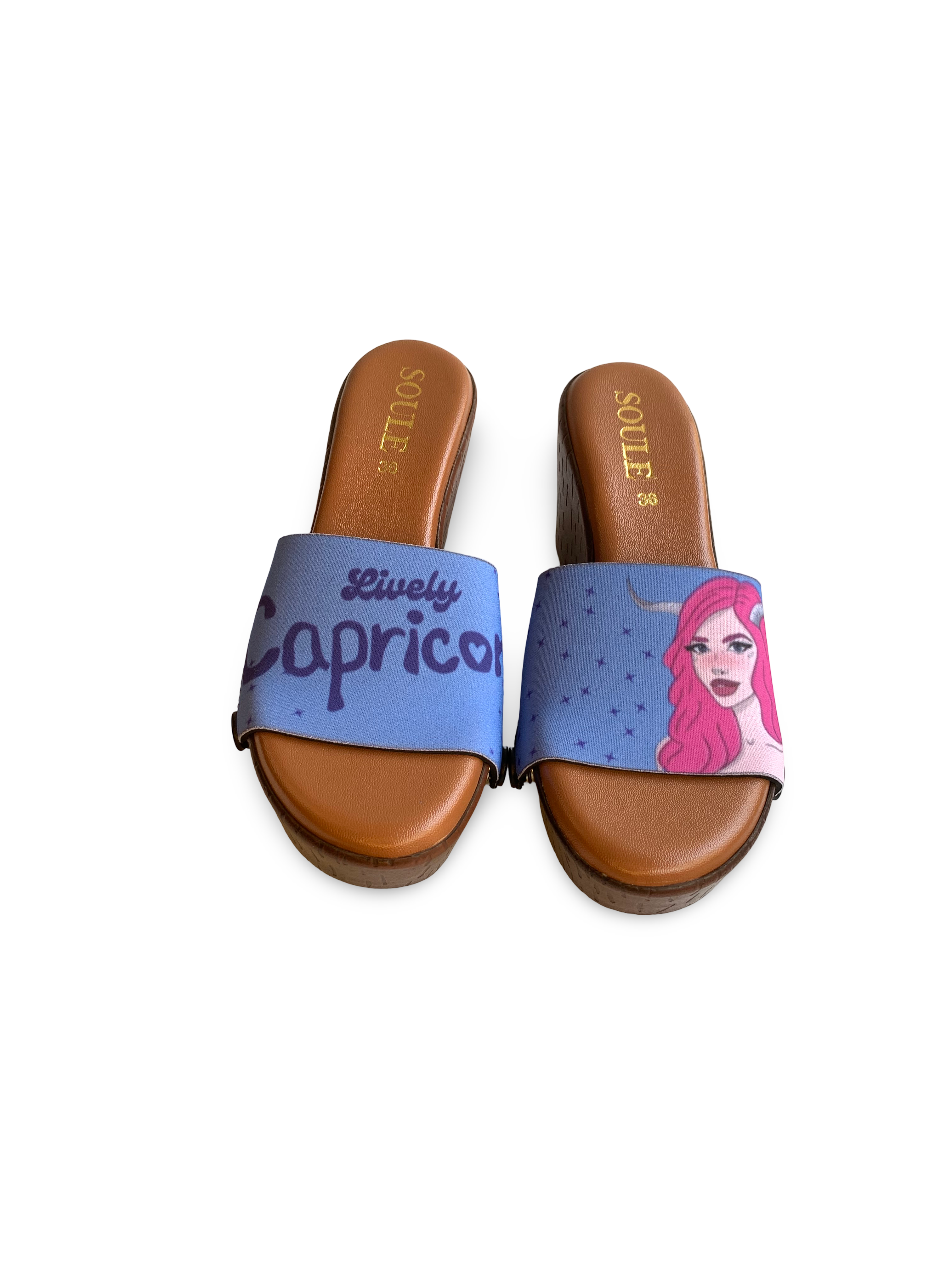 A pair of brown sandals with a Capricorn sign and a character with pink hair and a confident expression, along with the text 'Lively Capricorn' on the straps by Soule Footwear